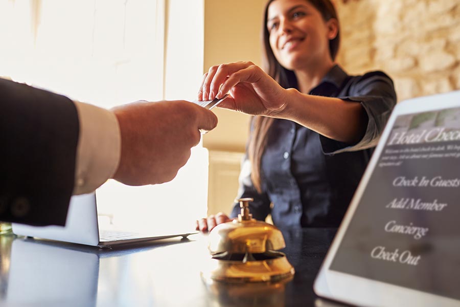 Specialized Business Insurance - Hotel Reception Desk With Woman Greeting a Guest, Handing Him a Keycard, With Information and a Brass Bell on the Desk